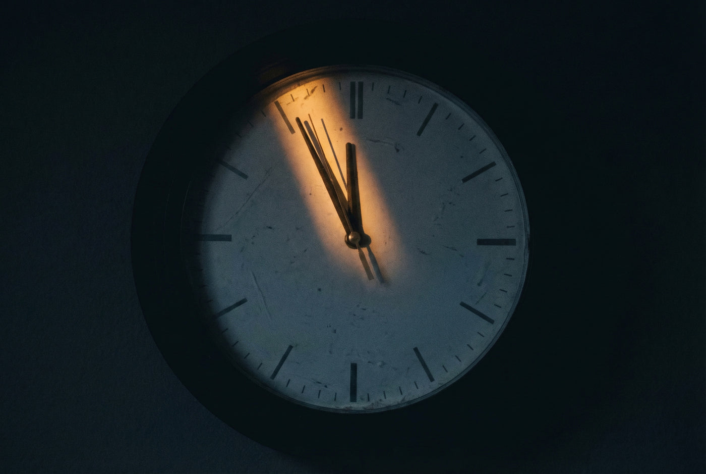 Orologio da parete al buio con un raggio di luce sulle lancette, quasi a mezzanotte